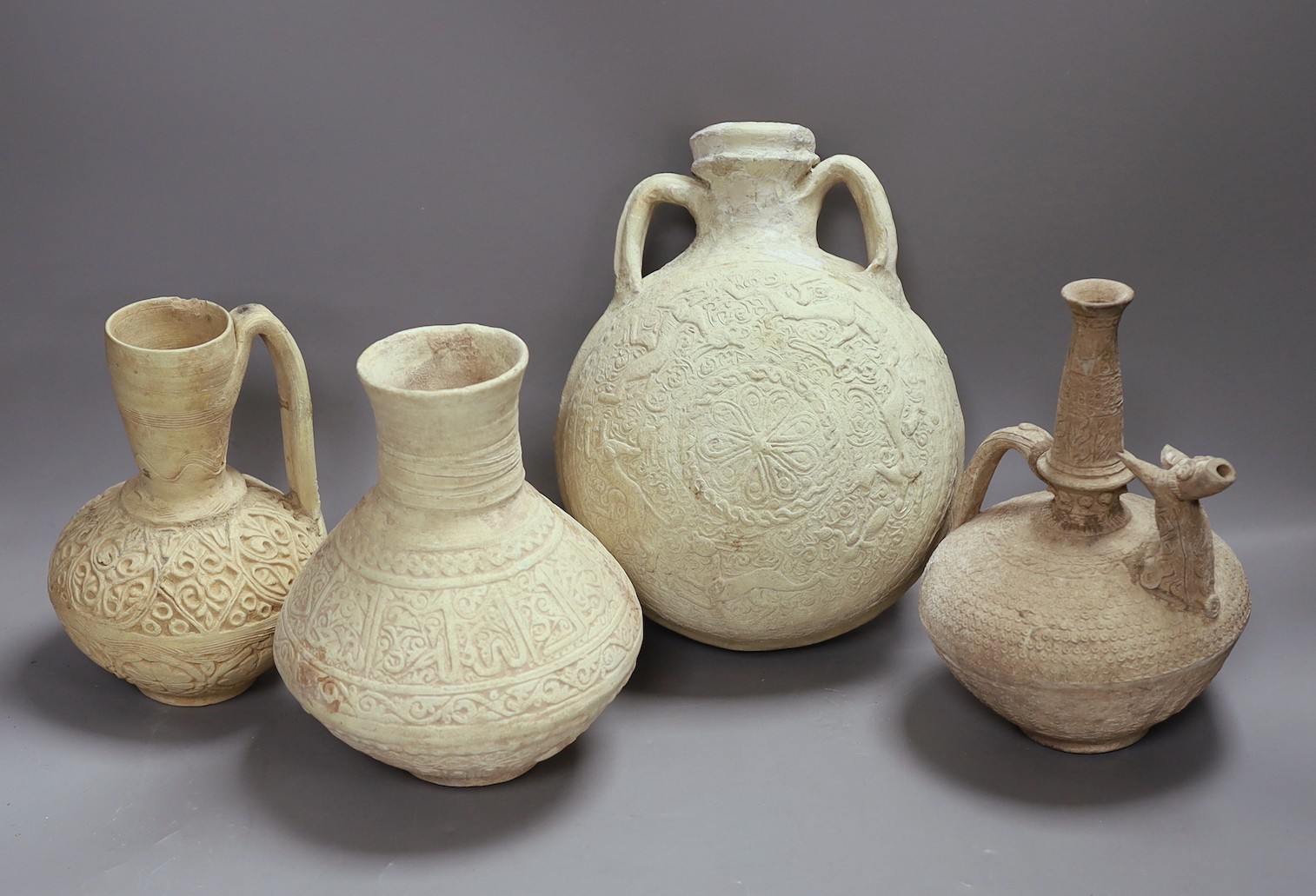 A group of Islamic terracotta vessels, Middle Eastern, possibly 12th century, including two jugs, an animal headed ewer and a two handled flask, The latter 25 cm high